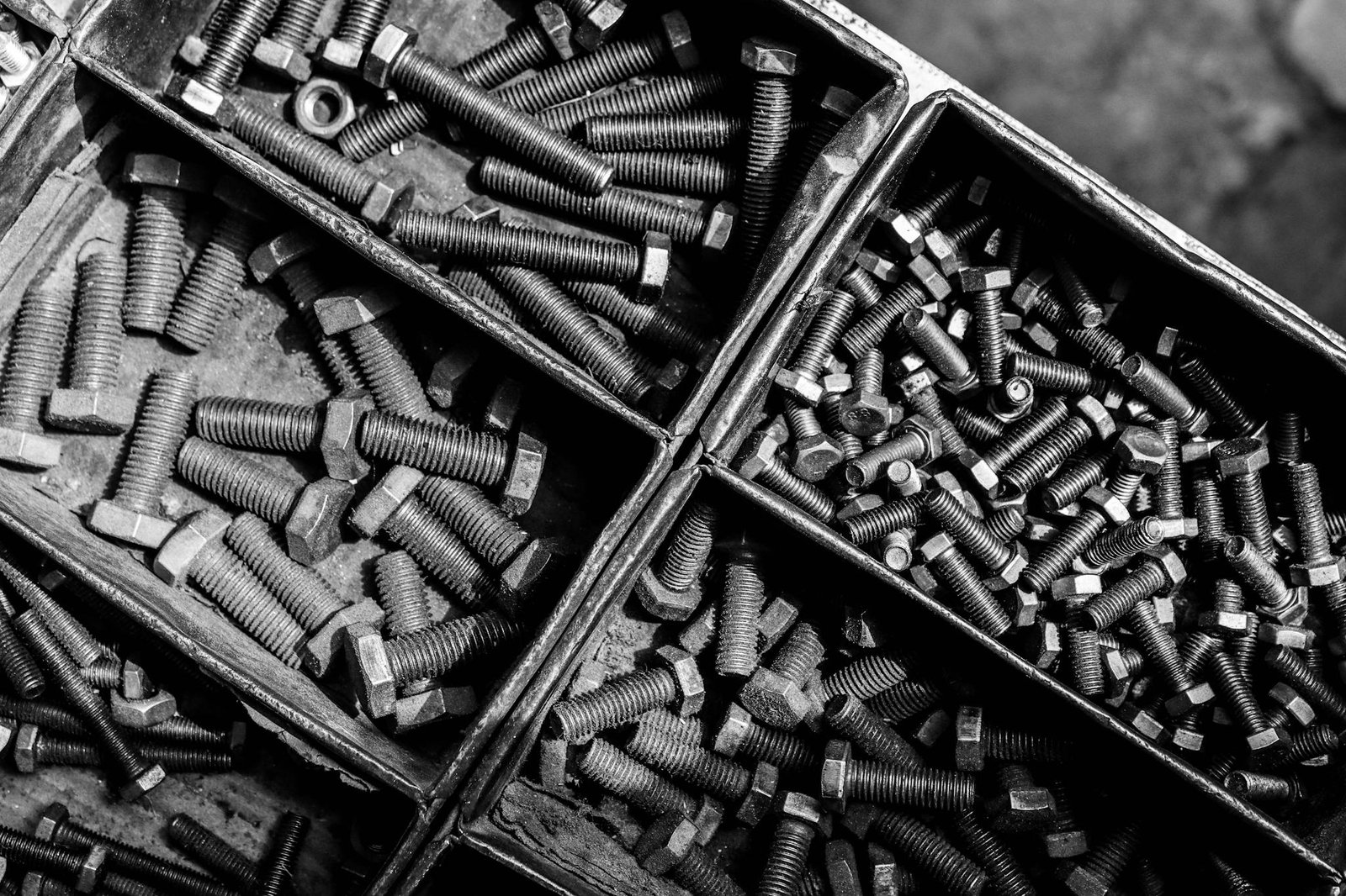 Black and white photo showcasing assorted bolts and screws in metal bins.