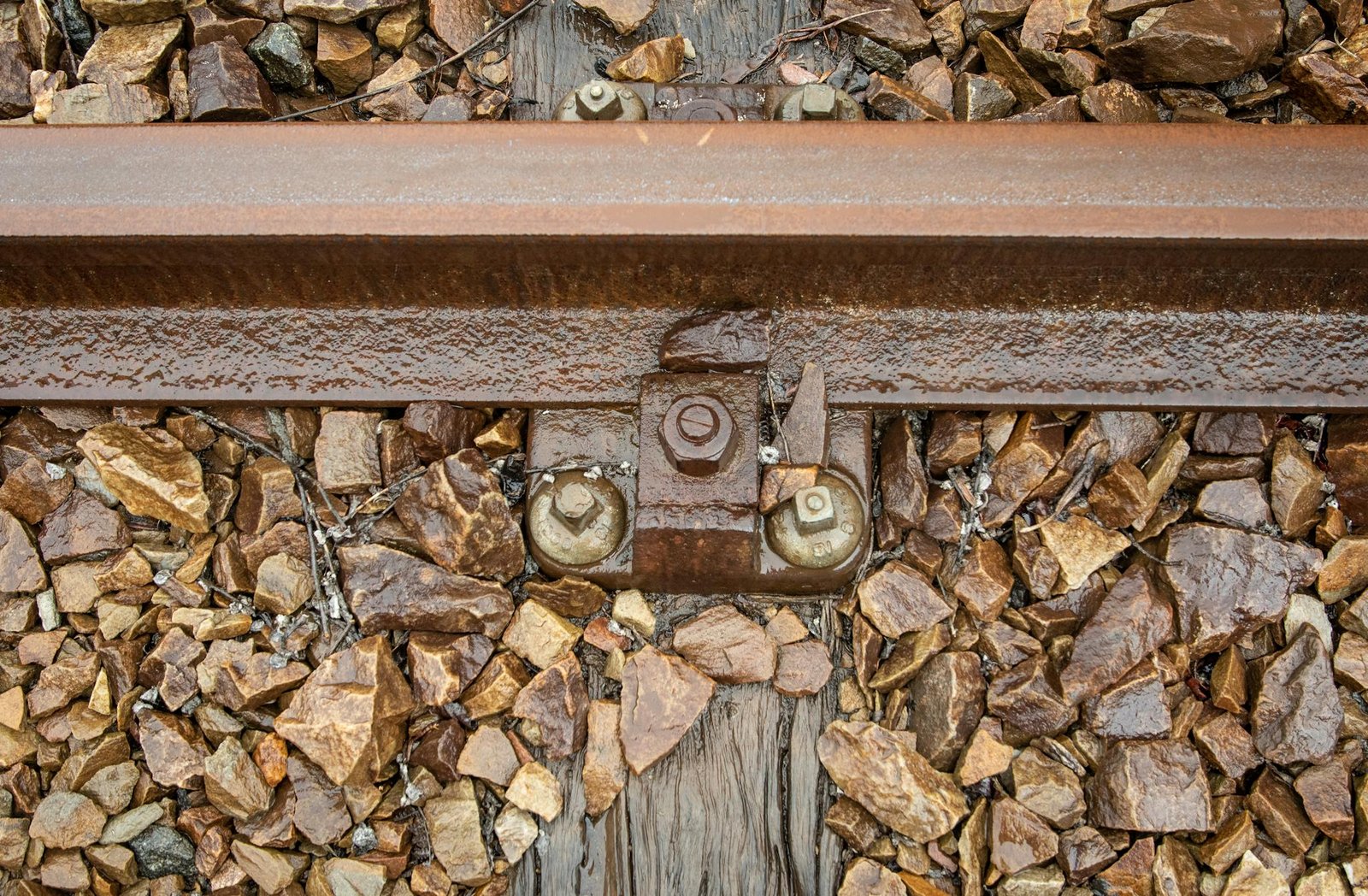 Detailed close-up of a rusty railway track surrounded by gravel stones.